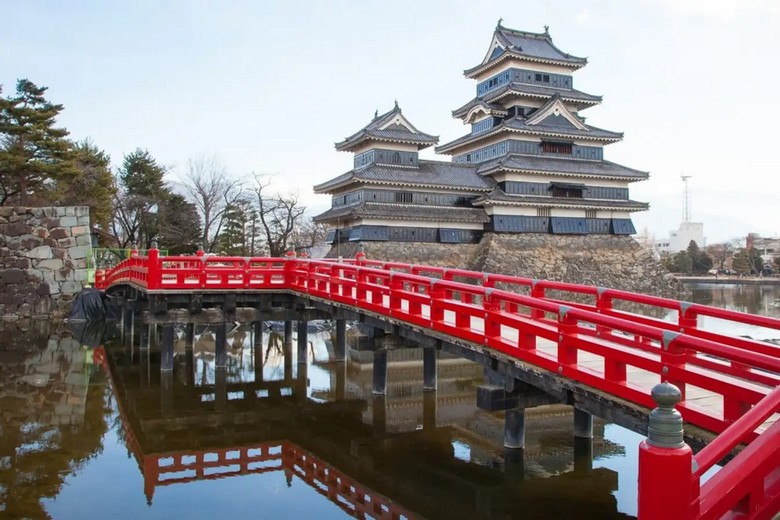 Lâu đài Matsumoto tường đen soi bóng trên hào nước với cầu gỗ đỏ