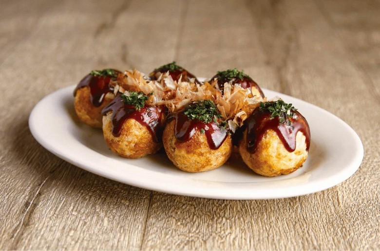 Hộp takoyaki 8 viên phủ sốt và cá bào, chụp trên nền gỗ hoặc đường phố